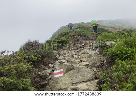 Tourist route mark on stone, painted in white and red guiding the way to the hiking mountain. Tourist hikers with backpack