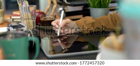 Side view of female designer working with digital tablet on black table with painting brushes and designer supplies