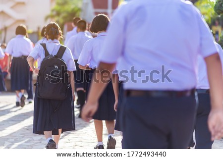The back view of Asian high school students in white uniform are walking towards preparing to respect the national flag in the morning amidst the beautiful nature surrounding the school.