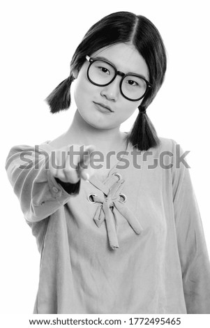 Studio shot of young beautiful Asian woman pointing finger at camera