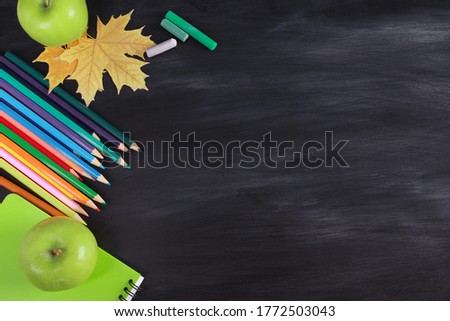 Colorful pencil and crayons, green apples, fall leaves, notebook on blackboard texture background. Top view, copy space, flat lay. Back to school in autumn, school supplies concept