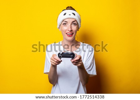 Young woman plays a virtual game with a joystick in her hands on a yellow background.