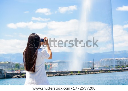 Asian beautiful woman is travel for holiday in the summer of Europe and taking a camera view landscape of lake and bright sky in Geneva Switzerland, copy space.