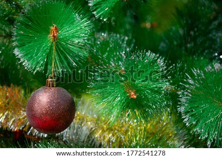 On the green Christmas tree hangs a large brown and gold Christmas ball: happy new year and Christmas! Close up. Christmas decor. New year greeting card