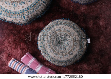 A circular pillow, embroidered with Arabic accent, on  dark red background
