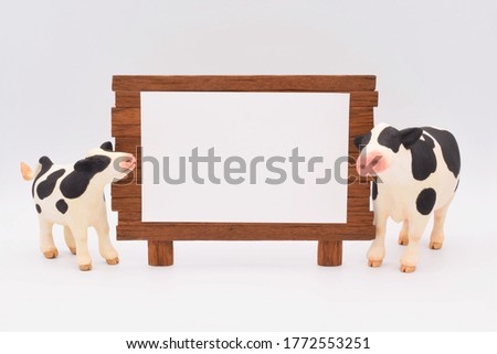 A cow parent and child sculpture made of clay against the background of the lawn. A wooden sign with white paper.
Horizontal position.