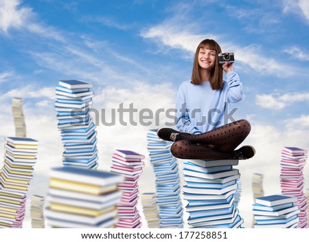 young woman taking a photo sitting on a high books tower