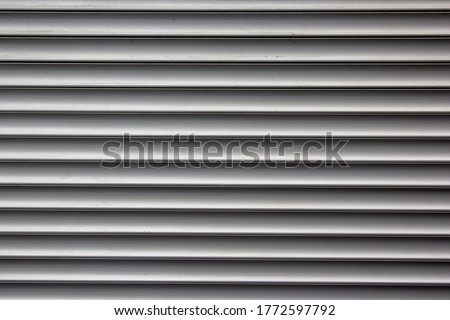 Background of grey horizontal metal strips. Roller blinds and garage gates. Closed metal shutter casements. Grey metal blinds with horizontal lines. Protecting windows and doors from intruders.