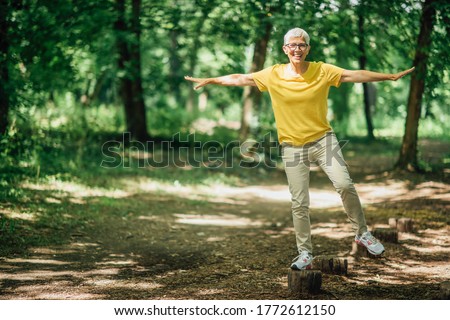 Balancing exercise outdoors. Mature woman standing on one leg, exercising balance  Royalty-Free Stock Photo #1772612150