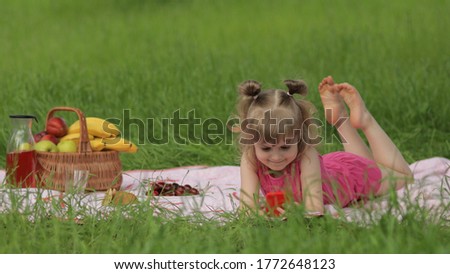 Weekend at picnic. Girl on grass meadow with basket full of fruits play online games on mobile phone. Child kid using smartphone for watching movies on internet. Chatting, social media network