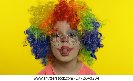 Child girl clown in colorful wig making silly faces. Happy five years old little caucasian kid having fun, smiling, dancing, looking at camera. Expressions. Halloween. Yellow background. Chroma Key