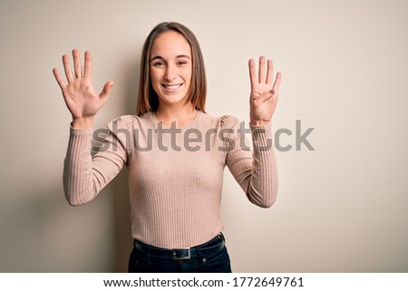 Young beautiful woman wearing casual sweater standing over isolated white background showing and pointing up with fingers number nine while smiling confident and happy.