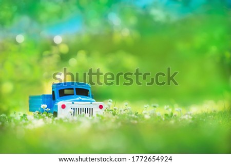 Blue toy car is on the green grass fiend. Old retro automobile for kids and games. Beautiful view for graphic wallpaper, background and backdrop  