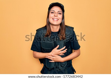 Young beautiful brunette policewoman wearing police uniform bulletproof and cap smiling and laughing hard out loud because funny crazy joke with hands on body.