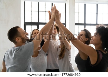 Head shot excited young mixed race sporty people joining hands in air, giving high five to each other, celebrating team success or self supporting before intensive workout in modern sport club. Royalty-Free Stock Photo #1772684930