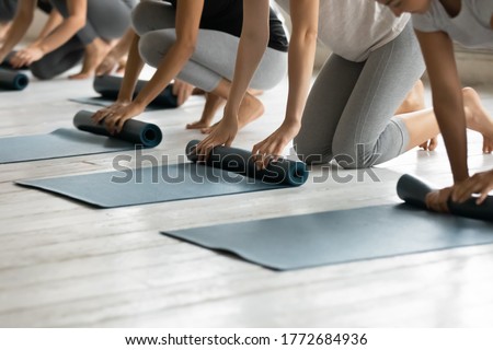 Close up young diverse barefoot people folding sport floor mats together, finishing yoga class lesson indoors, group of athletic friends unrolling rubber carpets, starting yoga workout at gym studio. Royalty-Free Stock Photo #1772684936