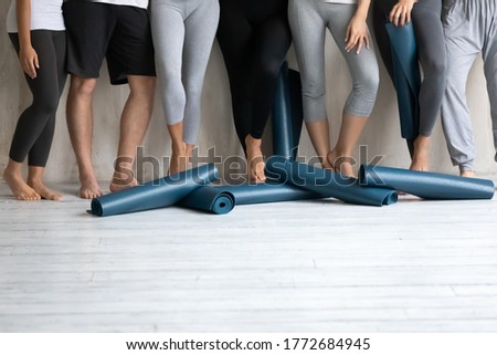 Close up multiethnic diverse people in sport pants and leggings standing barefoot near wall with sportive rubber mats on wooden floor, copy space for advertisement text, active lifestyle concept. Royalty-Free Stock Photo #1772684945