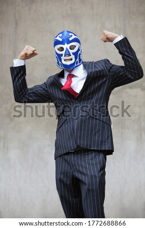 Young businessman flexing muscles in wrestling mask over gray background