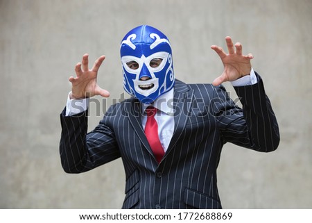 Young businessman gesturing in wrestling mask and pinstripes suit over gray background