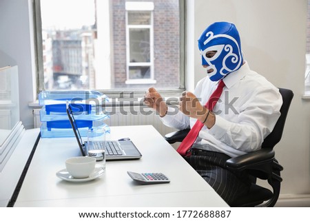 Young businessman celebrating victory in wrestling mask at office desk