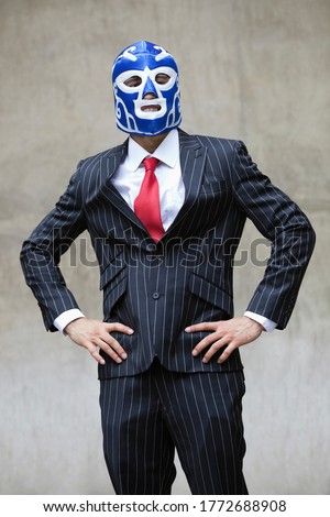 Young businessman in pinstripes suit and wrestling mask over gray background