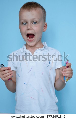 boy opening his mouth wide holding colored felt-tip pens on a blue background. High quality photo