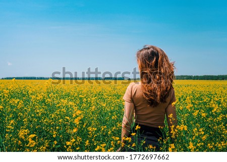 A woman with long hair walks in a rapeseed field, a photo taken from the back, the concept of flowering and summer day, a place for the text banner