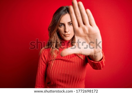 Young beautiful brunette woman wearing casual turtleneck sweater over red background doing stop sing with palm of the hand. Warning expression with negative and serious gesture on the face.