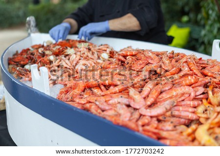 hundreds of prawns, shrimp and other shellfish inside of a small boat. On the background there is a couple hands refilling this huge plate. Royalty-Free Stock Photo #1772703242