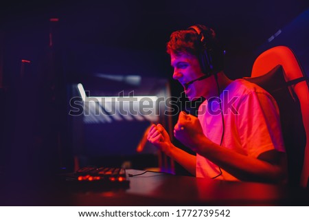 Gamer young man plays online video games computer and monitor wins tournament, rejoices and raises hands, neon color.