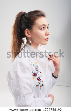 Close up portrait of 20-25 years old girl in a white blouse. Beautiful girl with a tail posing and not looking at the camera