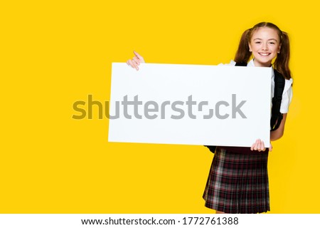 Schoolgirl student pupil holding big empty space white placard banner isolated yellow bright color background and smile