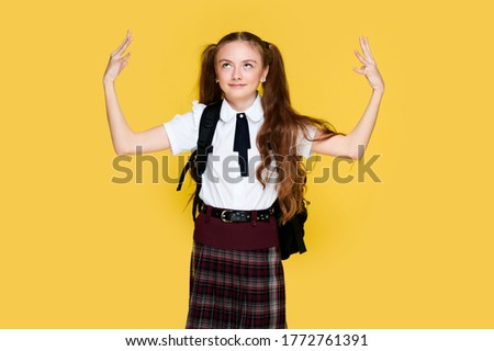 Young schoolgirl on bright yellow background holding hands and heads, student in uniform and backpack