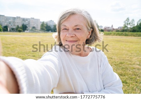 A beautiful European older woman makes a selfie. Elderly grandmother talking on video of communication on smartphone, waving her hand into the front camera