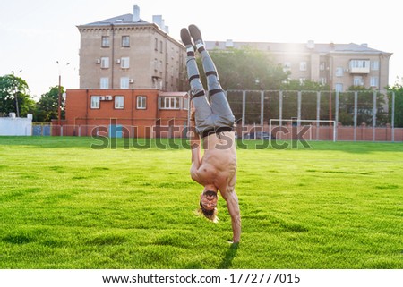 Standing on one hand upside down. Strong, muscular inflated extreme man. Young athlete of Caucasian nationality standing on the football field and doing different physical exercises.