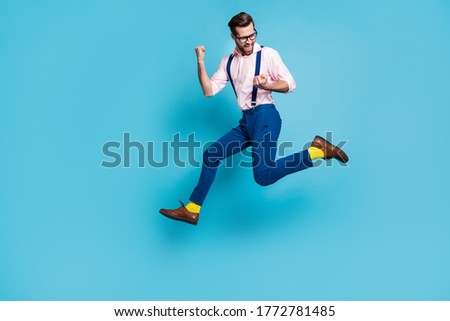 Full size profile photo of handsome man jump high up running competition raise fists first place winner race marathon wear specs shirt suspenders pants boots isolated blue color background