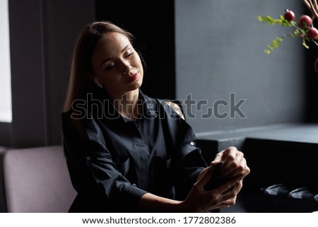 Stylish blonde girl with red painted lips and closed eyes wearing trendy black shirt sitting in cafe and listening music.                               