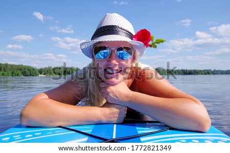 Blond woman with white hat, resting on paddleboard. The photo is taken in Sweden.