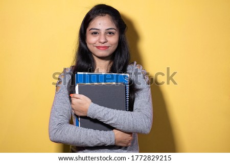 Smiling Indian female student holding books and file , college or school student and education concept isolated on yellow background with copy space.