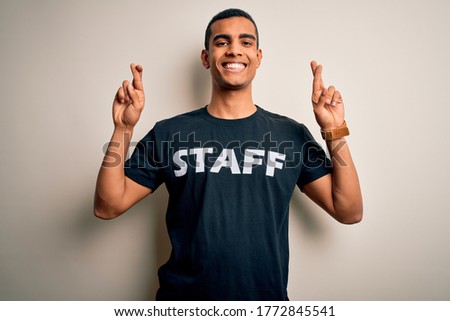 Young handsome african american worker man wearing staff uniform over white background gesturing finger crossed smiling with hope and eyes closed. Luck and superstitious concept.