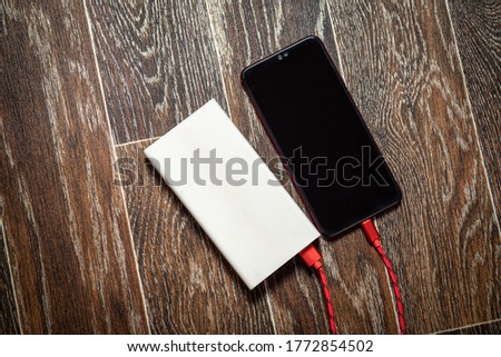 Smartphone charging with power bank on dark wooden surface.
