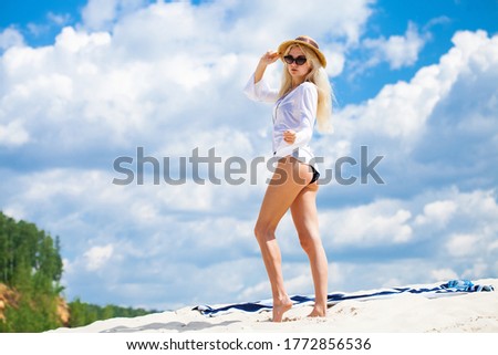 Portrait of a young beautiful blonde woman in a straw hat and sunglasses posing against a blue sky