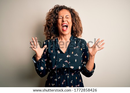 Middle age beautiful woman wearing casual dress standing over isolated white background celebrating mad and crazy for success with arms raised and closed eyes screaming excited. Winner concept