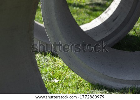 Massive concrete rings lay on green grass, abstract industrial photo background