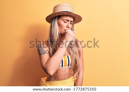 Young beautiful blonde woman wearing bikini and summer hat over isolated yellow background feeling unwell and coughing as symptom for cold or bronchitis. Health care concept.