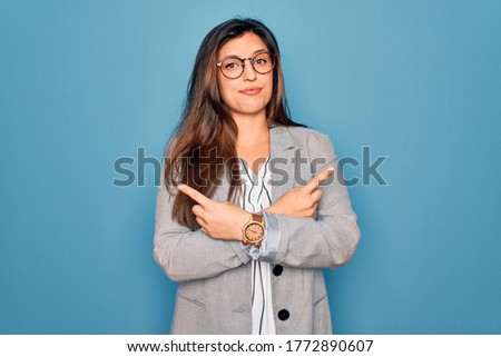 Young hispanic business woman wearing glasses standing over blue isolated background Pointing to both sides with fingers, different direction disagree