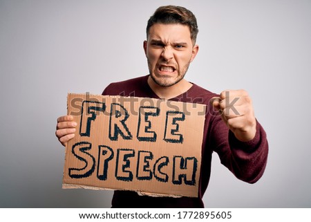 Young man with blue eyes holding banner on protest for free speech asking for free communication annoyed and frustrated shouting with anger, crazy and yelling with raised hand, anger concept