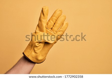 Hand of caucasian young man with gardener glove over isolated yellow background counting number 4 showing four fingers