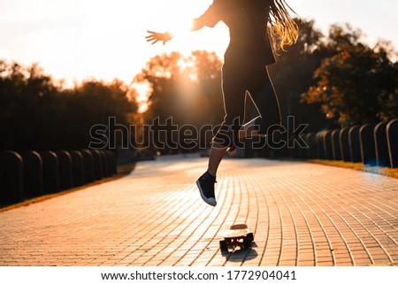 silhouette of a girl in gym shoes jumping on a skateboard in the setting sun in the park