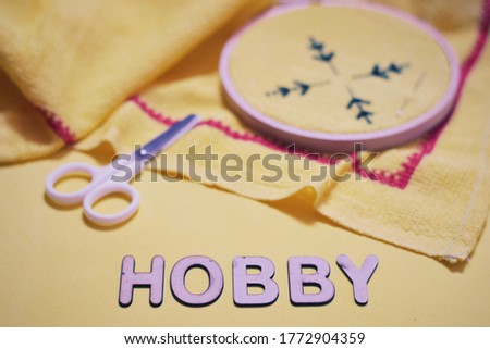 Word saying hobby made with 3d wooden alphabet letters laid on yellow background along with ongoing cross stitch embroidery sewing set. Selective focus.